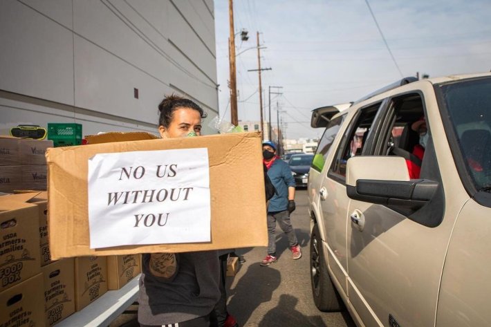 A volunteer with No Us Without You carrying a box labeled with the organization's name.