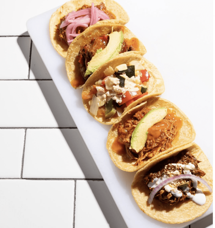 Five different tacos laid lengthwise on corn tortillas