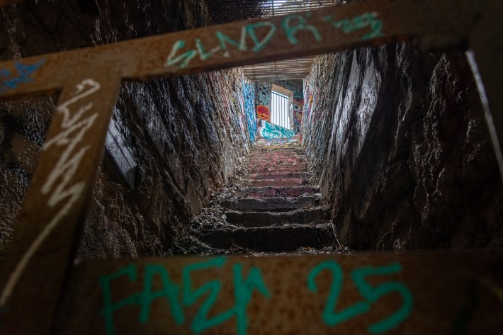 Stairs descending from the Lower Old Zoo Trail into one of the animal enclosures, with a spraypainted barrier in the foreground, a door with bars up above.