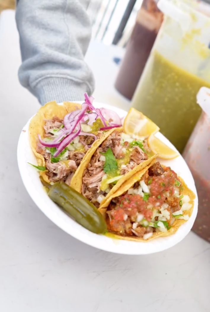 Carnitas tacos topped with red salsa, pickled red onions and lemon.