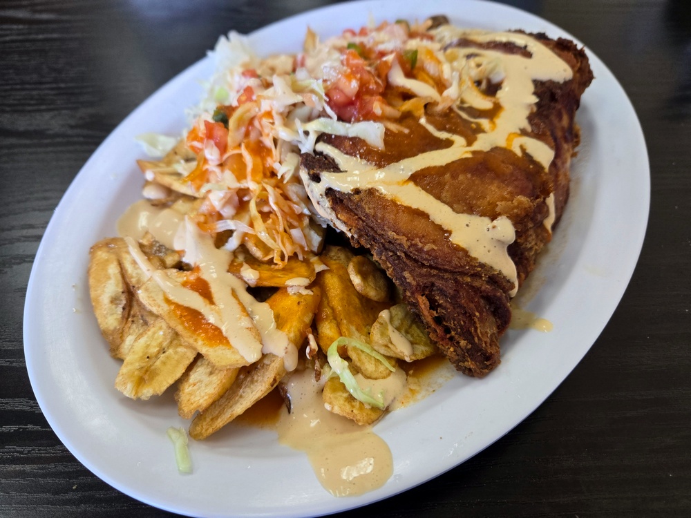 A huge leg and thigh of fried chicken drizzled in light yellow sauce, with plantains and cabbage