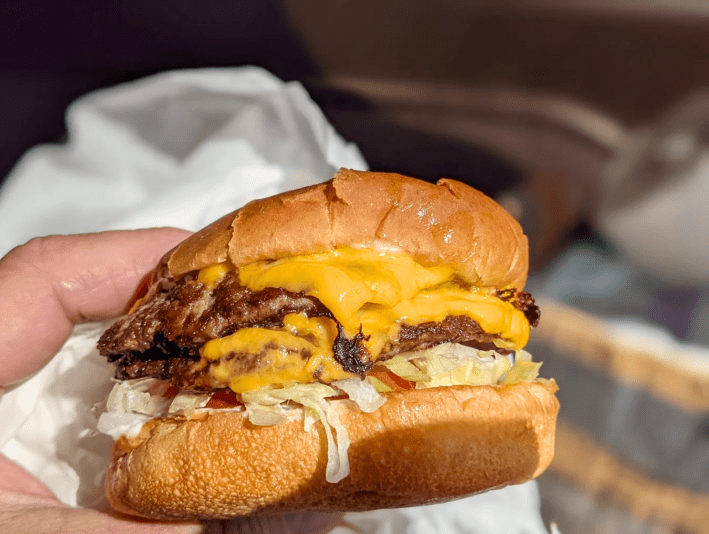 Double cheese burger with shredded lettuce and tomato on toasted buns from Bill's Burgers.
