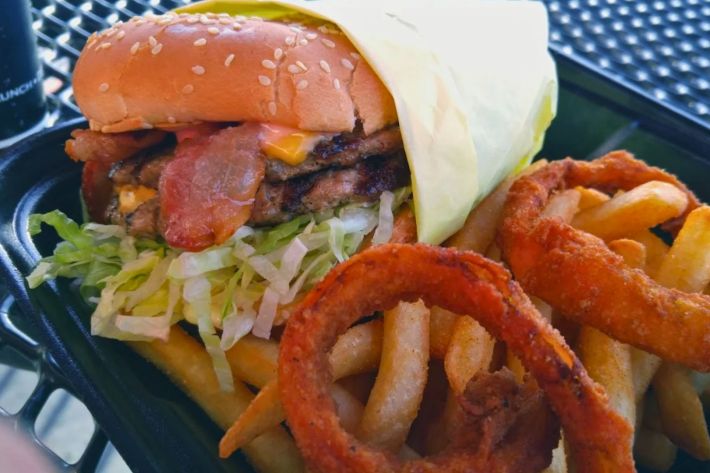 Double cheese burger with bacon, lettuce and tomato, with a side of fries and deep fried onion rings.